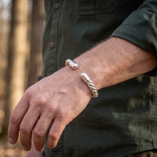 Twisted rope coil arm ring in a polished silver finish worn on a man's wrist, rounded terminals catching the light in woodland