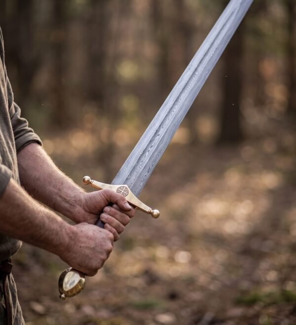 Two hands gripping a Damascus arming sword with engraved brass guard and brass pommel in an autumn forest