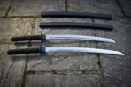 Two piece daisho set of katana and wakizashi with black handles laid on flagstones below their two black lacquered saya