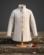 Front view of an undyed linen padded gambeson with vertical quilting and a row of tied cord loops, on a stand with a coiled cord and belt beside it