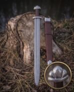 Valknut hilt viking sword standing upright at a woodland stump beside its strapped brown leather scabbard, the Damascus fuller and polished steel throat clearly visible