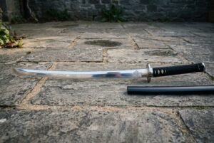 Valknut katana with three interlocked triangles etched at the blade base, a polished steel tsuba and black cord over white rayskin resting on grey stone paving