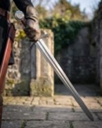 Viking arming sword with engraved disc pommel and etched serpent line held point down by a gloved hand