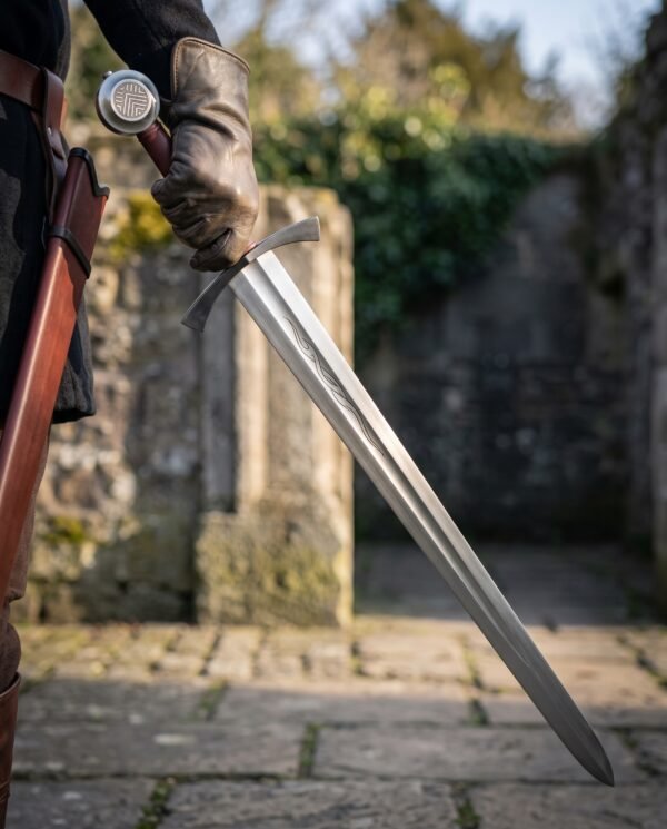 Viking arming sword with engraved disc pommel and etched serpent line held point down by a gloved hand