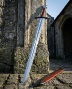 Viking arming sword with russet leather grip, black guard and etched serpent line leaning on a stone pillar