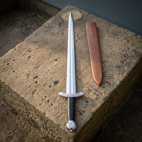 Viking dagger with a leaf shaped double edged blade, knotwork cut guard and steel disc pommel lying on a weathered sandstone block beside a tan sheath