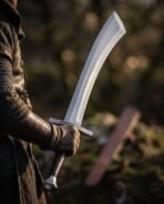 Viking scimitar with flared curved blade and black leather grip held at the hip by a figure in mail and dark leather