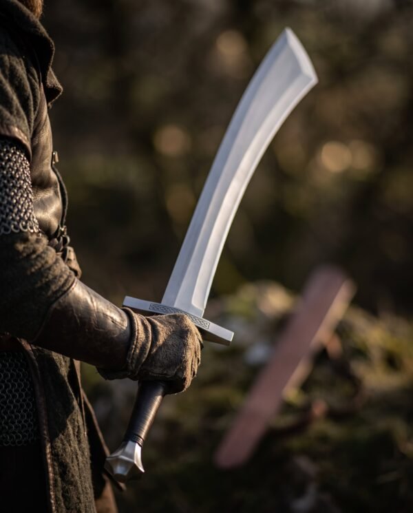 Viking scimitar with flared curved blade and black leather grip held at the hip by a figure in mail and dark leather