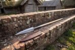 Viking spear with leaf shaped steel head and long ash haft lying on an old brick wall beside its brown leather sheath