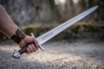 Viking sword with etched knotwork panel and lobed pommel held out at arm length over a gravel path