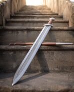 Viking sword with pattern welded chevron fuller and lobed steel pommel leaning on stone steps over its brown scabbard