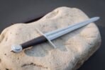 Viking sword with runes along the blade, dark leather grip and polished wheel pommel resting on a limestone rock