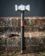 Walnut haft war hammer with a double faced polished steel head, engraved blackened collar and black leather grip standing upright against a mossy red brick wall