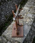 Walnut sword display stand with felt lined brass tipped cradles seen from the side on top of an old stone wall