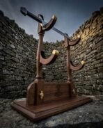 Walnut two tier sword display stand with brass capped cradles and Mjolnir engraving holding a sword inside a stone wall
