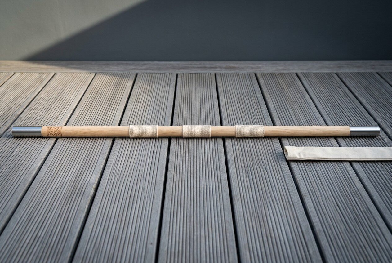White ash bo staff with polished steel end ferrules and three whipped cord grip bands lying across grey timber decking b White ash bo staff with polished steel end ferrules and three whipped cord grip bands lying across grey timber decking beside its canvas carry sleeve