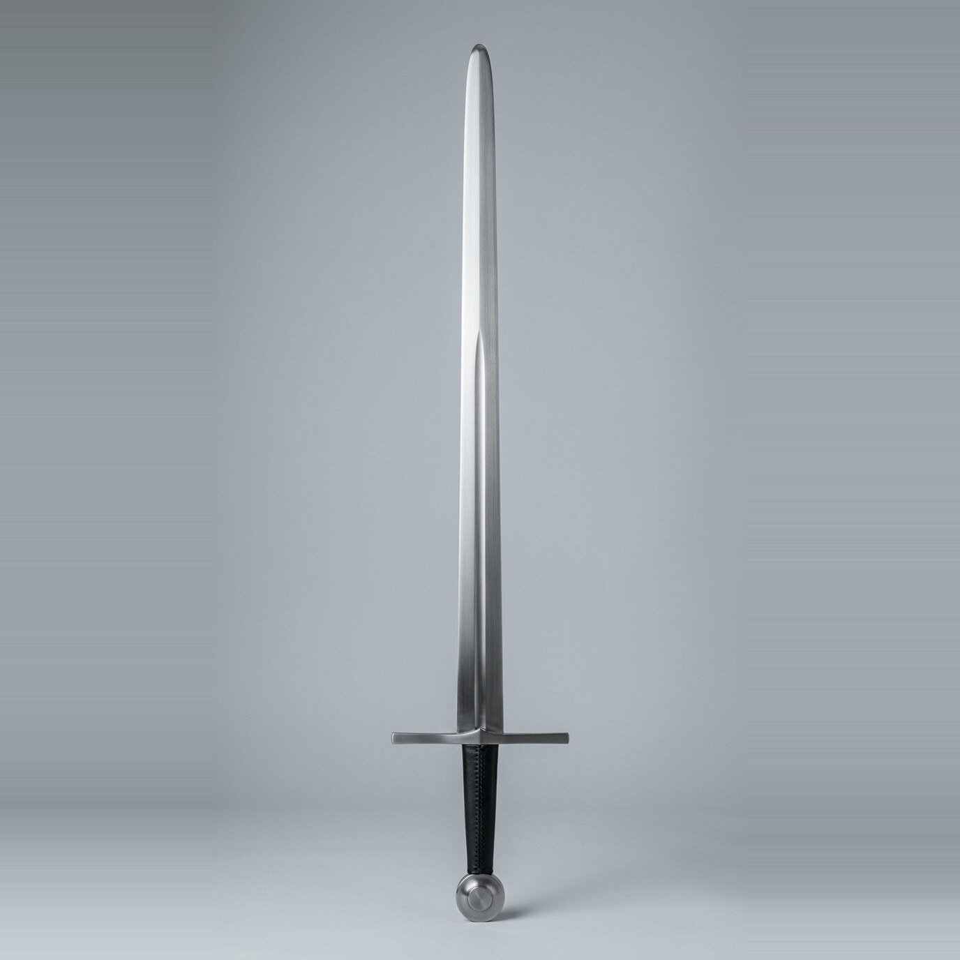 Draugmar wide fuller arming sword trainer Wide fuller arming sword trainer with a plain straight cross, a fuller running two thirds of the blade, black leather seam grip and bossed wheel pommel laid on a plain grey studio backdrop