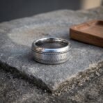 Wide rune ring with twisted rope borders and engraved futhark band lying on its side on a sandstone ledge beside an oak tray