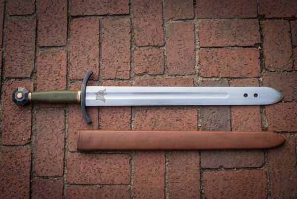 Wolf etched arming sword in polished high carbon steel with a blackened curved guard, olive green leather grip, faceted pommel and leather scabbard on red brick paving