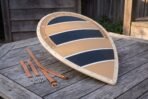 Wooden kite shield painted with navy and tan bands and a tooled knotwork border lying on a garden table with leather straps